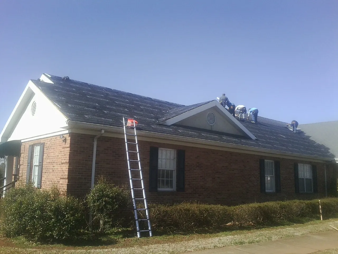 Crew tearing shingles off a brick ranch roof with a ladder set — Emergency Roof Repair work by our crew in Free Union