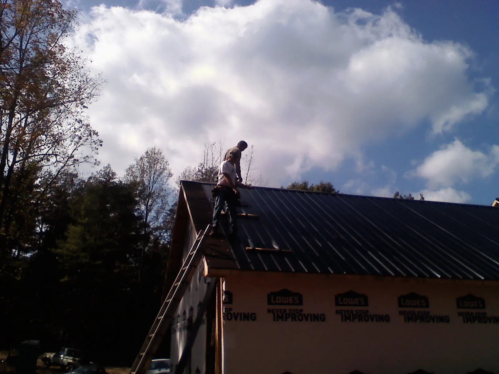 Roofer fastening dark metal panels high against a cloudy sky, from a Roof Inspection job in Free Union